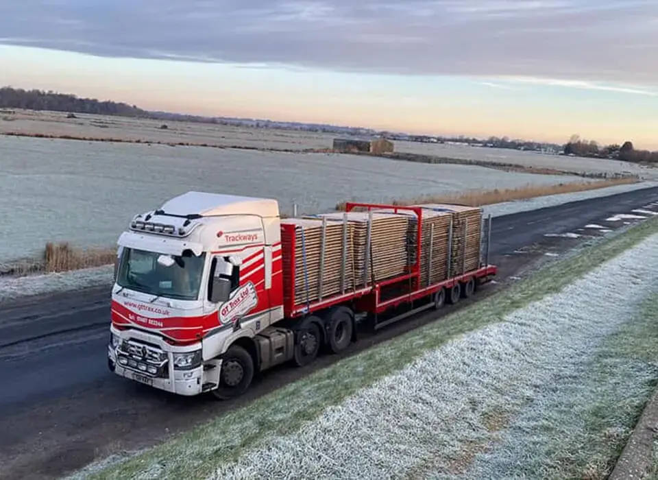 White and red GT Trax truck hauling stacked PowerTrax 60 panels on a rural road with frost-covered fields.